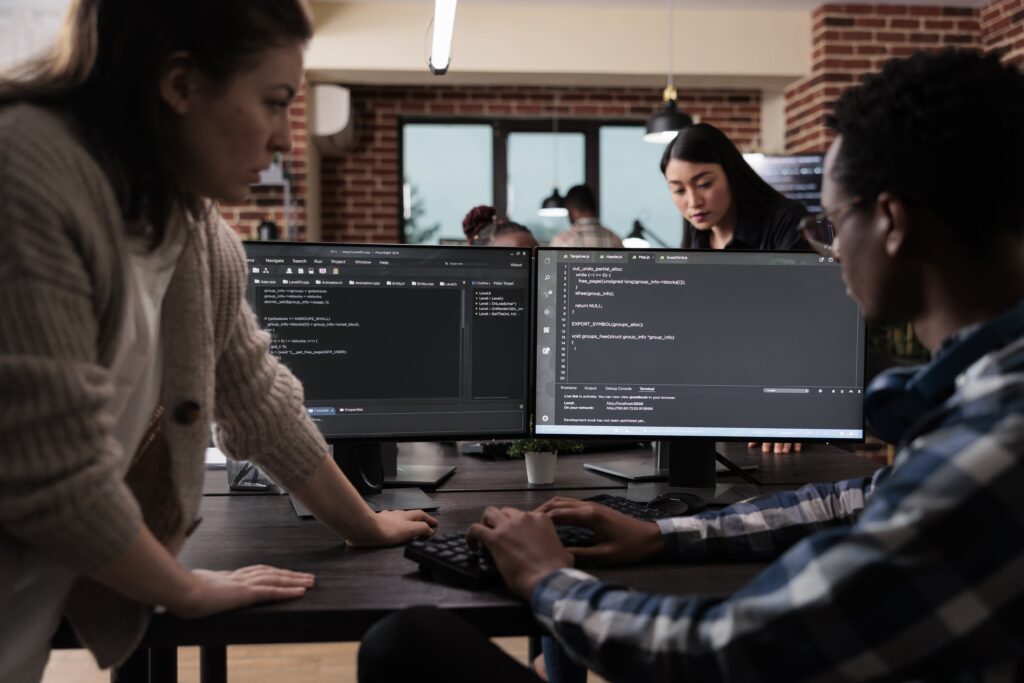 Cover image of the content about 'Internal Developer Platforms Pain Points', where programmers are discussing in a workspace with multiple screens displaying programming code.