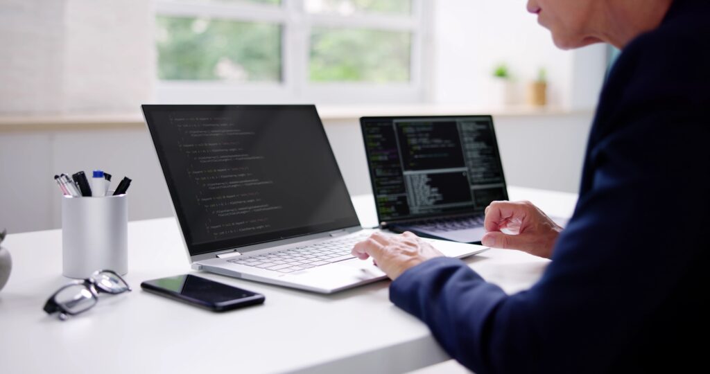 Image cover of the content Latest trends in platform engineering for engineering leaders, where there is a woman working on a notebook with codes. To her right side, there is another notebook, and to her left, there are glasses, a pen holder, and a cellphone.