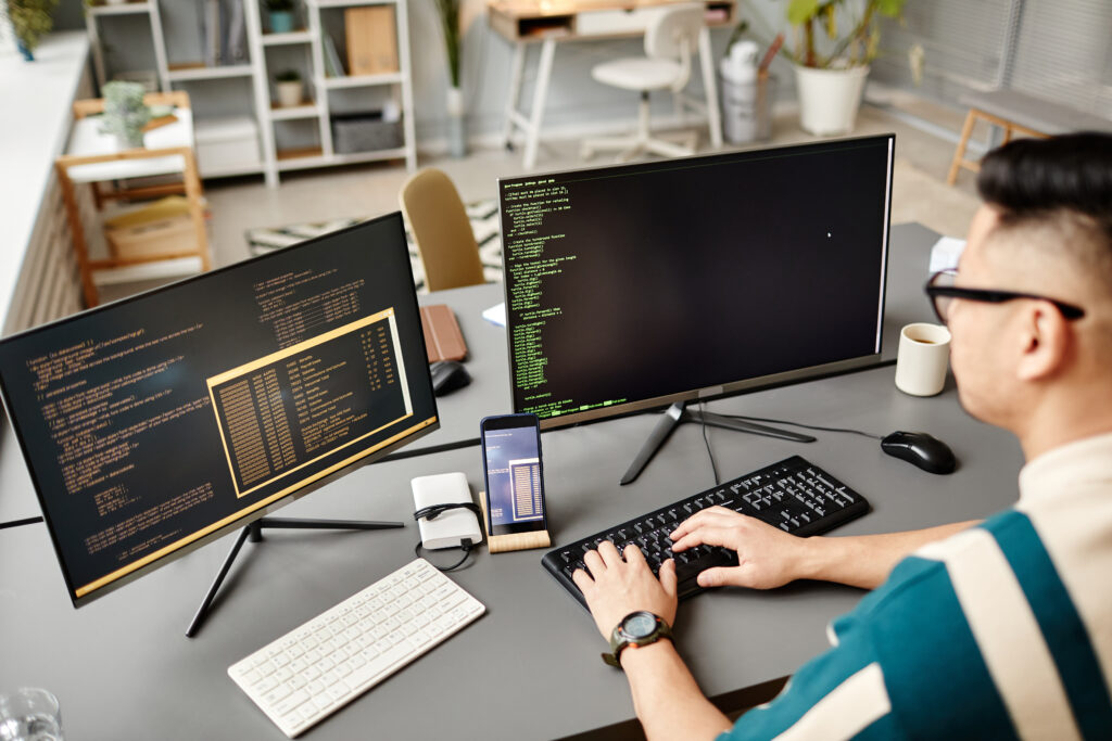 Capa do artigo com uma foto de uma pessoa de características asiáticas em frente ao computador, ela possui dois monitores e dois teclados em cima da mesa. As mãos da pessoa está em um dos teclados.