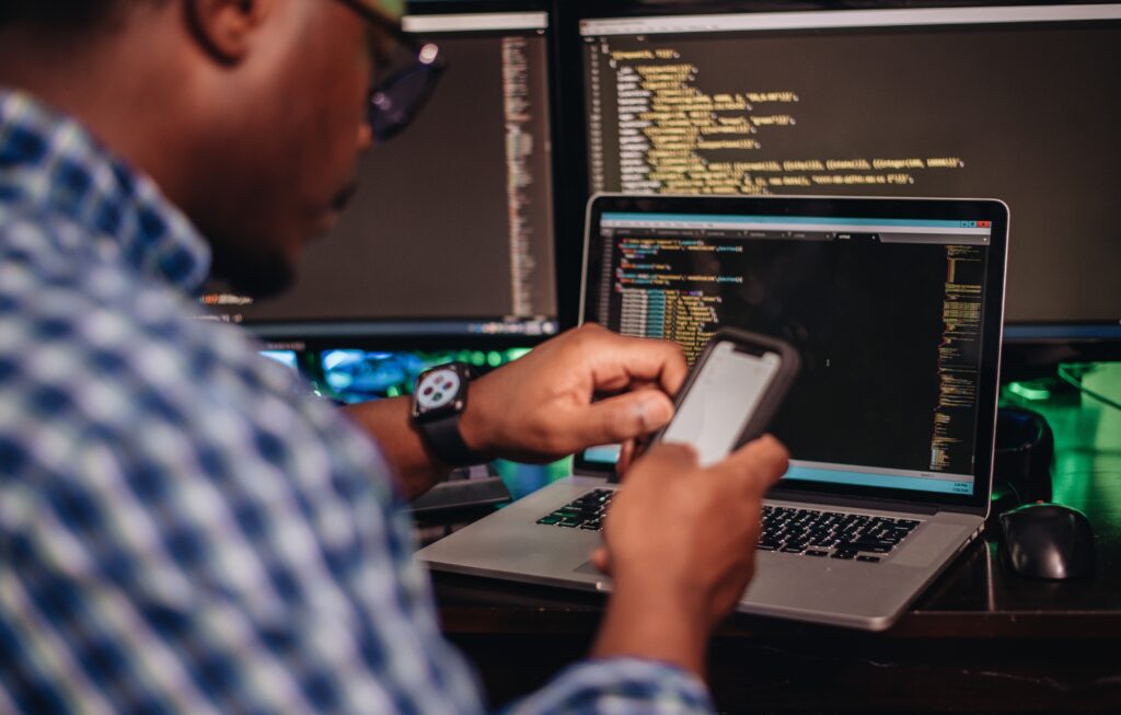 Cover image of the content about how Developer Platforms are transforming development, featuring a man using a mobile phone in front of computer screens filled with code.