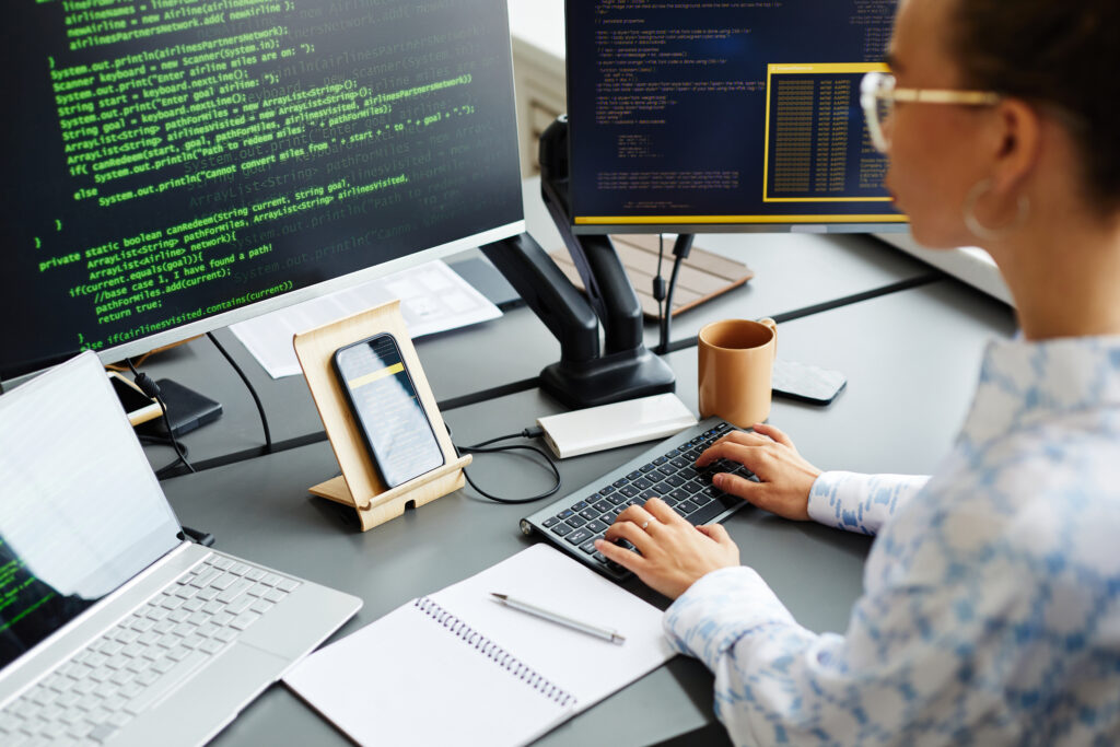 Imagem capa do conteúdo sobre padrões e antipadrões da engenharia de plataforma, onde há uma Mulher programando em frente ao computador. Na mesa, aparecem duas telas e um celular.