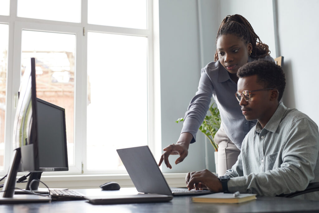 Cover image for the content on legacy software modernization, featuring two people collaborating in an office setting with two computer screens and a laptop on the desk.