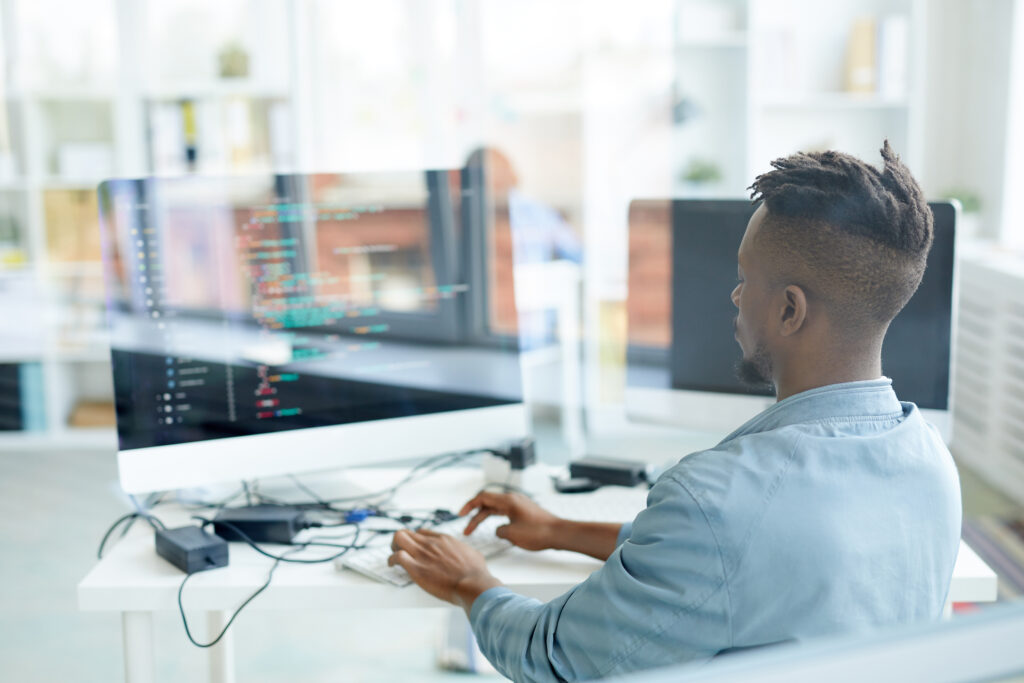 Homem negro está na frente de um computador com códigos na tela.